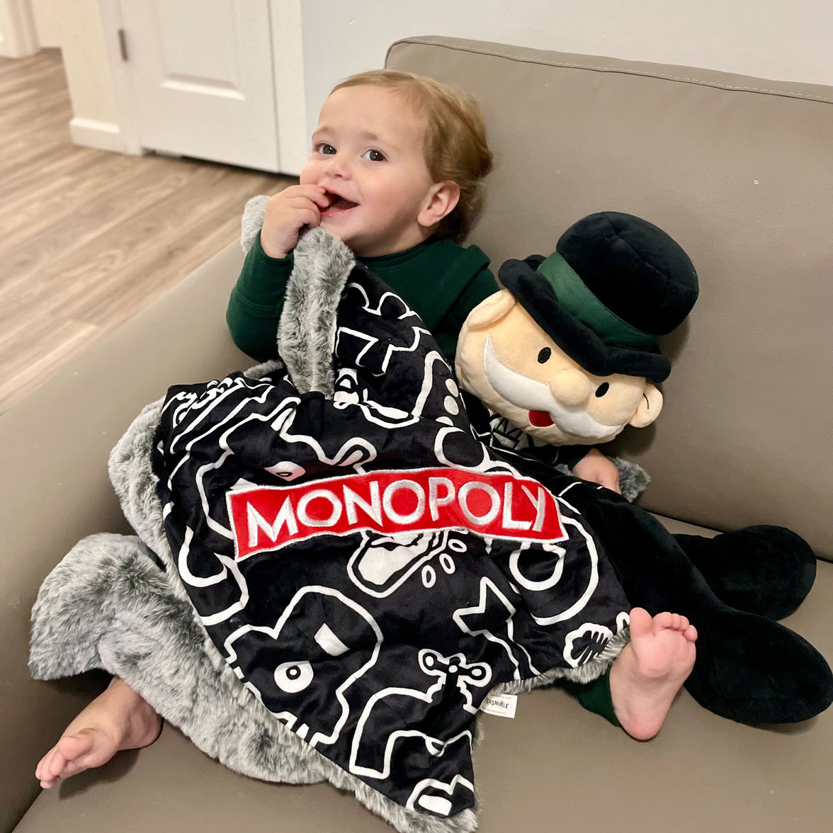 Child with a Monopoly-themed blanket and plush toy on a couch.