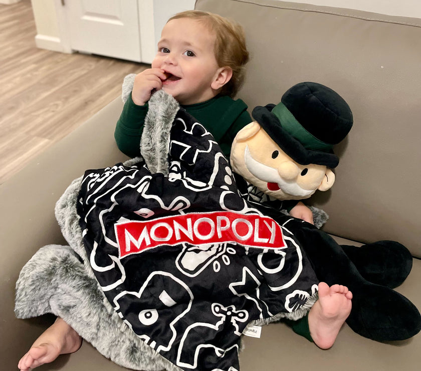 Child with a Monopoly-themed blanket and plush toy on a couch.